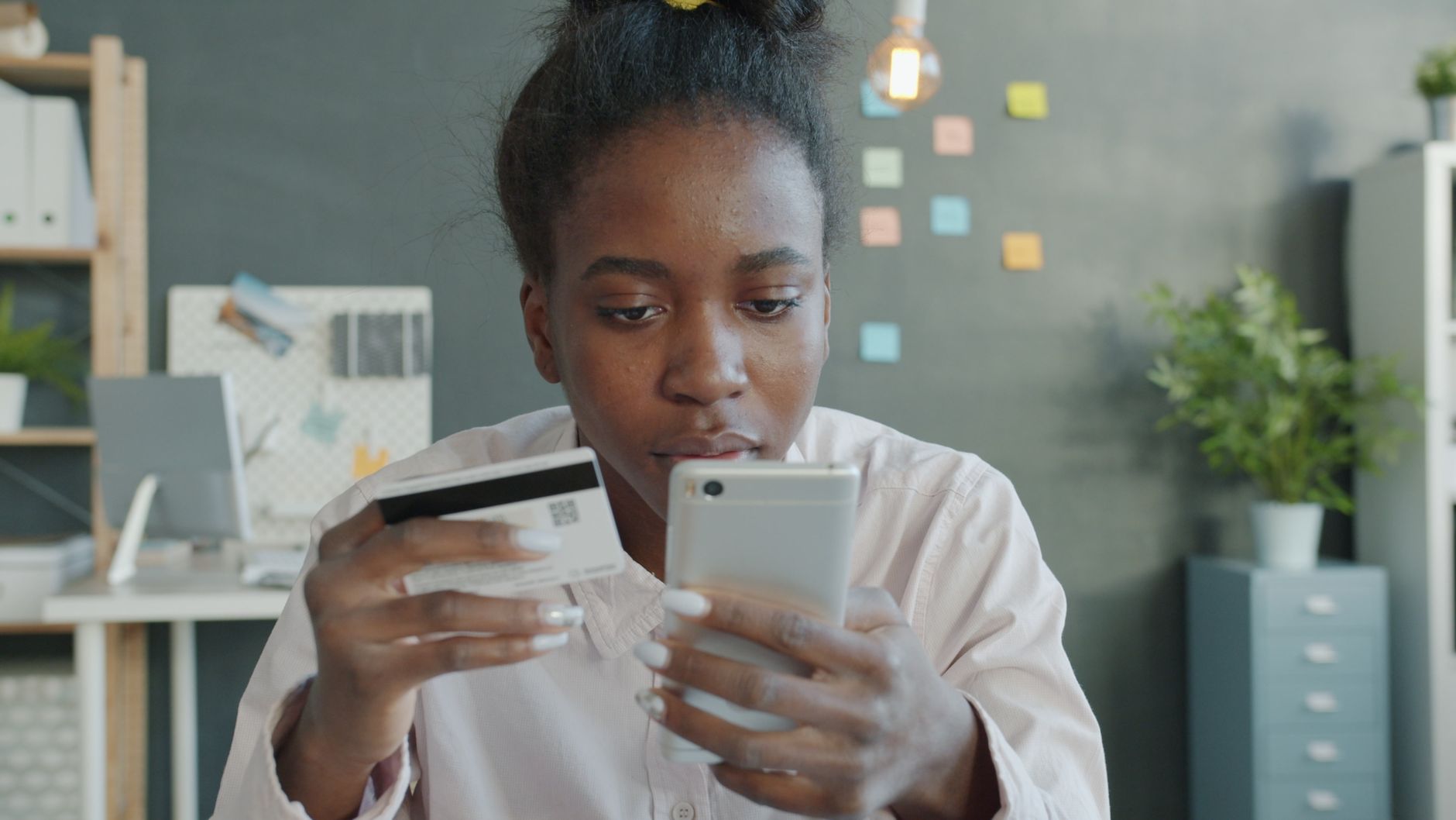 Nigerian woman holding a bank card while using a smartphone to manage Facebook ad payments