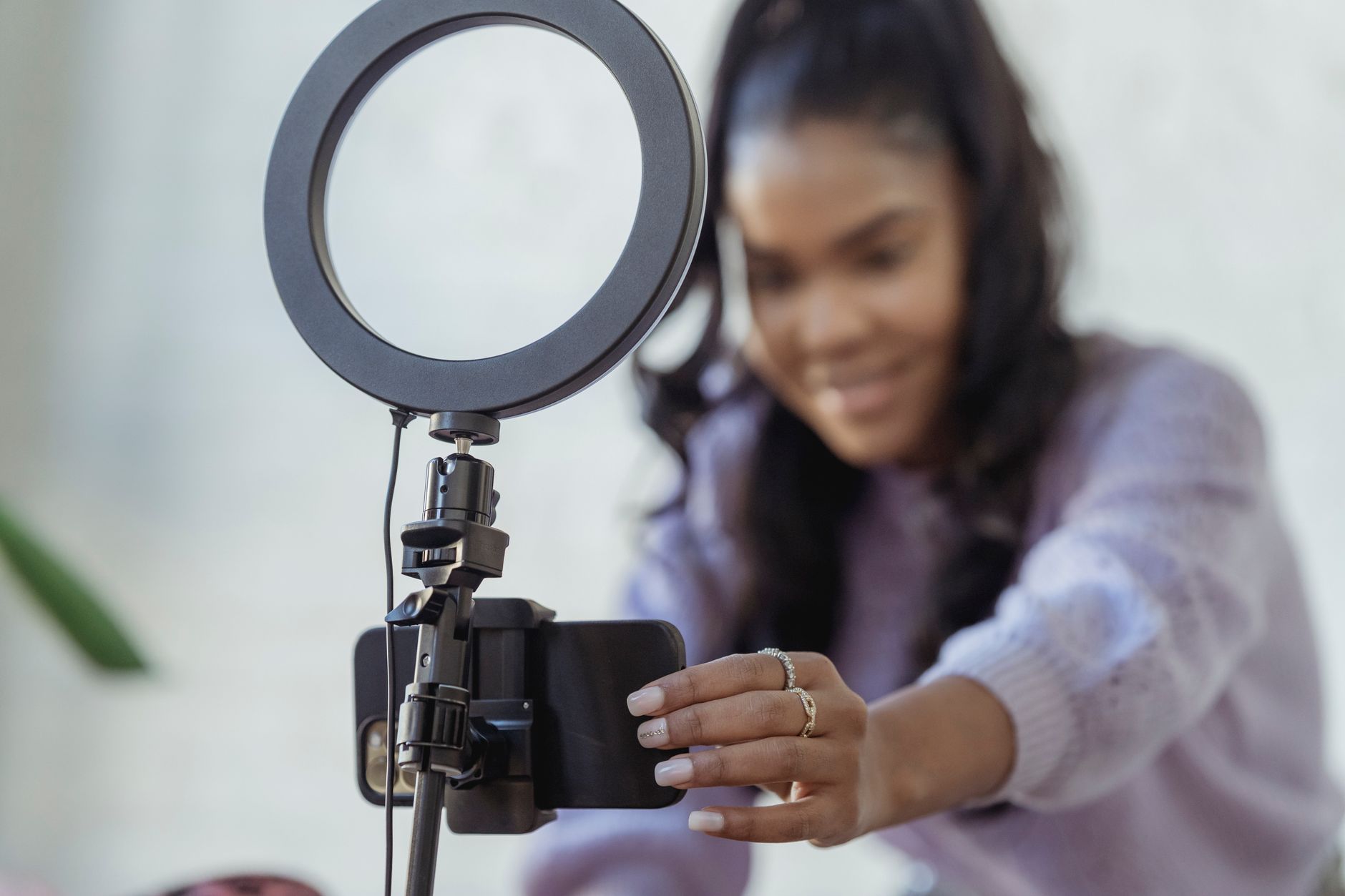 Young African American female content creator setting up smartphone on ring light tripod to film TikTok video