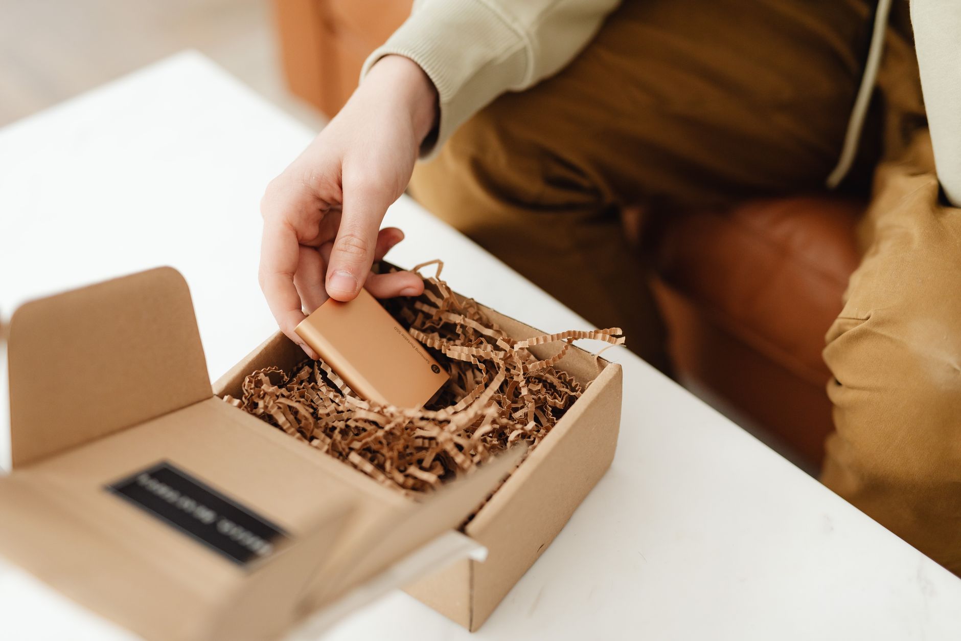 Person unboxing a small product from a kraft cardboard delivery package filled with crinkle paper