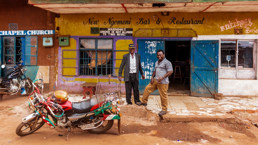 Two men standing outside an African bar and restaurant with a visible painted storefront sign