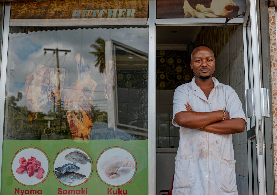 African small business owner standing confidently at his shop storefront with business signage visible
